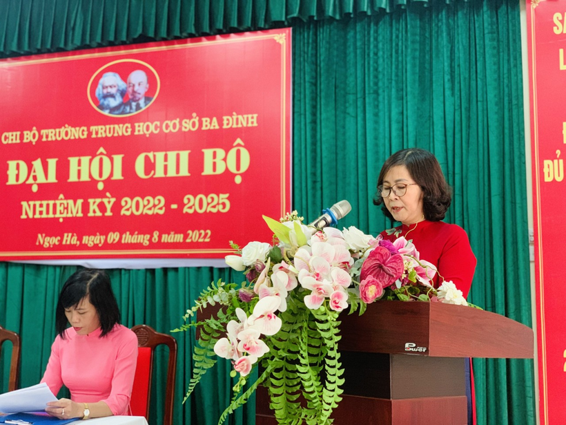 A person standing at a podium with flowers in front of a signDescription automatically generated with low confidence