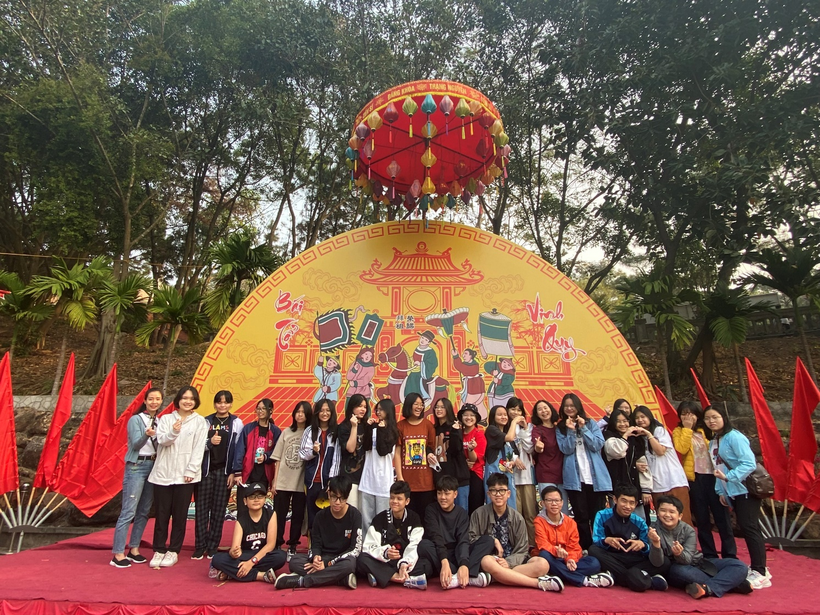 A group of people posing for a photo in front of a large yellow and red structureDescription automatically generated with low confidence
