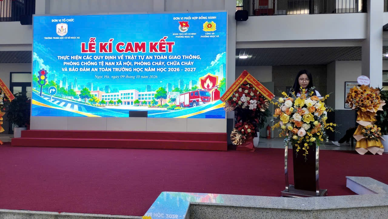 A person standing on a podium with flowers in front of a large sign

Description automatically generated